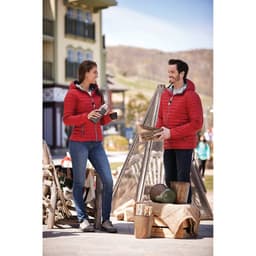 A red packable insulated jacket for women, displayed on a model outdoors, featuring a hood and a logo.