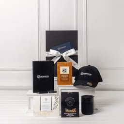 A gift pack featuring a black cap, notebook, candle, and assorted packaged items, all presented in a sleek box with a bow.