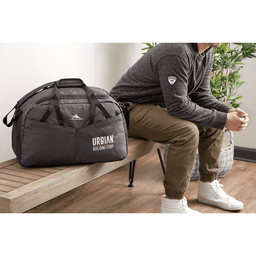 A dark grey duffel bag with a logo, placed beside a person sitting on a bench in a modern setting.