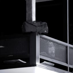A black duffel bag rests on a balcony railing, featuring a logo and sturdy handles.