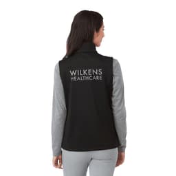 A black women's softshell vest with a high collar and grey long sleeves visible underneath, featuring a logo on the back.