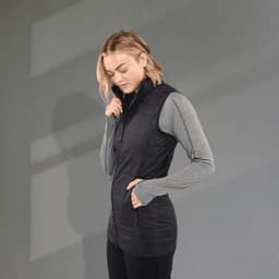 A woman wearing a black lightweight packable insulated puffer vest over a grey long-sleeve top, with hands in pockets.