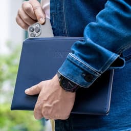 A navy tablet case is held by a person, with a smartphone partially visible inside the case. The image features a logo.