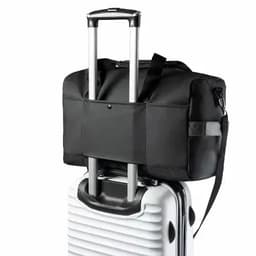 A black duffle bag with a strap, resting on the handles of a white suitcase. The bag has a logo.
