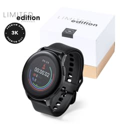 A black fitness smartwatch with a circular display, packaged in a white box with a gold base and logo.