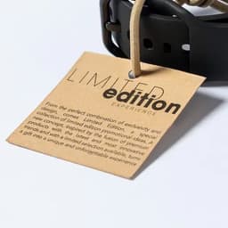 A brown tag with a text description, attached to a black product strap, with a branding logo.