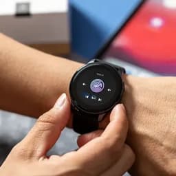 A smartwatch with a circular display, featuring a music player interface, worn on a person's wrist.