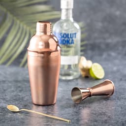 A drink bottle and jigger in a copper finish, with a bottle of vodka and lime in the background.