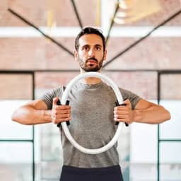 A man holds a white exercise ring with black grips, standing in an indoor fitness space.