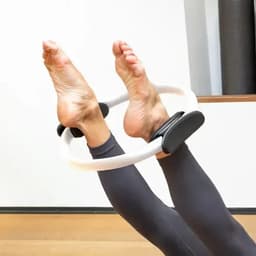 A fitness ring rests on the feet of a person in workout attire, with bare feet visible. The ring is white with black accents.