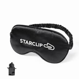 A sleep mask in black fabric with an adjustable strap and a logo. Includes a small pouch for storage.