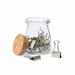 A glass jar with a cork lid containing silver metal binder clips, some are placed outside the jar.