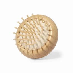A hairbrush with a round, gold body and wooden pins, featuring a textured grip and a smooth base. It includes a logo.