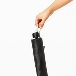 A black umbrella being held by a hand, featuring a circular handle for easy carrying.