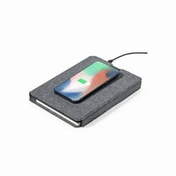 A grey notebook with a smartphone charging on top, connected by a cable. The notebook features a textured cover.