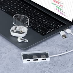 A charging hub with USB ports sits on a desk next to wireless earbuds and a laptop, all in sleek white design.