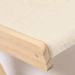 A close-up of a wooden edge with a smooth surface, featuring a light cream fabric underneath.