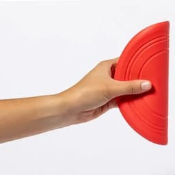 A red silicone kitchen tool being held in a hand, featuring a curved design for easy grip.
