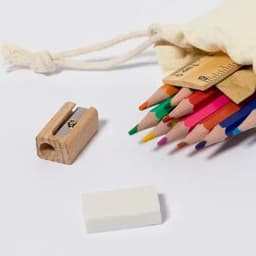 A drawstring bag contains coloured pencils, a wooden sharpener, and an eraser, arranged on a white background.