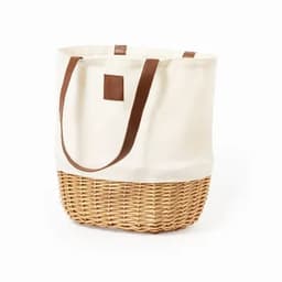 A tote bag with a cream canvas upper and woven, natural brown basket base, featuring brown leather handles.