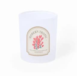 A clear glass container featuring a floral design and logo, predominantly in soft pink and cream colours.