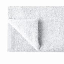 A white bath towel folded at one corner, featuring a textured surface and a neat edge. It includes a logo.