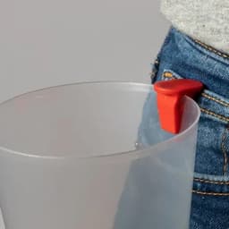 A drink bottle with a clear body and a red cap, positioned next to a pocket. It has a logo on the side.