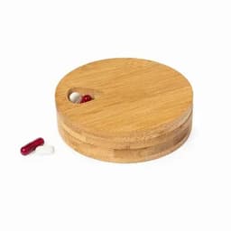 A round bamboo pill box with a small opening, featuring two capsules outside in red and white.