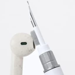A dental tool with a brush tip is positioned near a white earbud in the image. Both items are shown against a plain background.