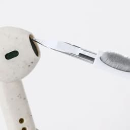 A cleaning tool is being used on a white and green wireless earbud, showcasing its detailed design.