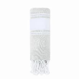 A rolled towel in shades of grey and white featuring fringe detail at the ends, with a broad white band.