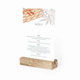 A menu card displayed on a wooden stand, featuring floral designs and various food categories like salads, soups, and desserts.