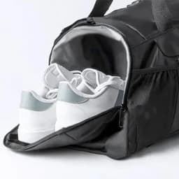 A duffel bag in black with a compartment displaying white and light blue shoes inside. The bag features zippers and handles.