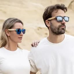 A pair of stylish sunglasses with blue lenses and wooden frames, worn by a woman and a man in casual white shirts.