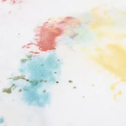 A textured surface featuring splashes of blue, red, green, and yellow colours on a white background.