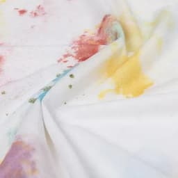 A fabric featuring a white base with vibrant, multicoloured splashes in hues of yellow, pink, green, and purple.