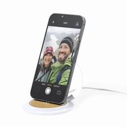 A smartphone on a circular wooden charging pad, displaying a selfie of two people in outdoor attire.