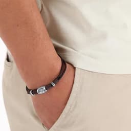 A leather bracelet with metal accents is worn on a wrist, displayed against a light-coloured shirt and pants.
