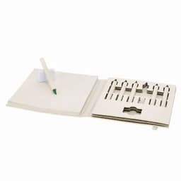 A notebook with a pen resting on it, featuring cut-out sections for crayons or coloured pencils. Light-coloured pages.