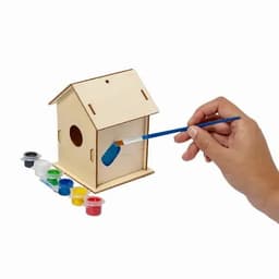 A wooden birdhouse being painted with a brush, surrounded by different pots of paint in various colours.