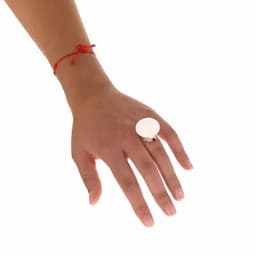 A hand wearing a silver ring with a large circular flat surface, accompanied by a red string bracelet.