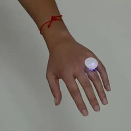 A hand wearing a large, illuminated ring with a round, white bulb and a blue base.
