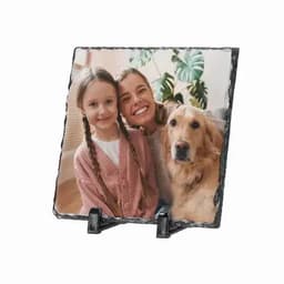 A framed photo on a decorative stand featuring a girl, a woman, and a golden retriever, set against indoor plants.