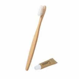 A bamboo toothbrush with soft bristles alongside a small tube of toothpaste. The items are in natural tones.