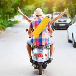 A scooter with a rider wearing a hat, holding a yellow drink bottle, while speeding down a sunny street.