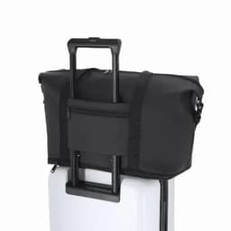A black duffle bag resting on a wheeled suitcase, featuring a front zipper pocket and adjustable straps.