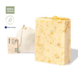 A bar of vegan soap with yellow and white tones, alongside a small fabric bag. It has a natural, textured appearance.