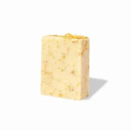 A bar of soap in cream colour with embedded natural herbs and floral elements. The soap has a textured surface.