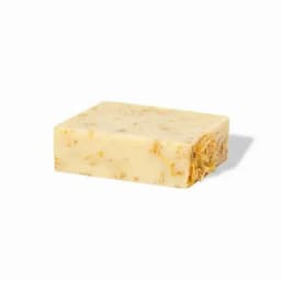 A bar of natural soap with a creamy yellow colour, featuring visible herbs and floral fragments embedded within.