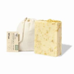 A natural shampoo bar with a creamy yellow hue and floral inclusions, accompanied by a small fabric pouch.